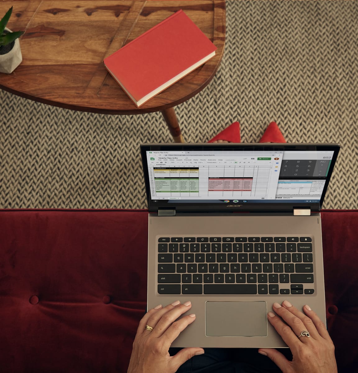 Una mujer con zapatos rojos sentada en un sillón del mismo color en el lobby de un hotel trabaja con una Chromebook.